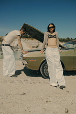 Pleated White Jeans worn by two models with a vintage Dodge Challenger at a chalk quarry — Confession Road campaign
