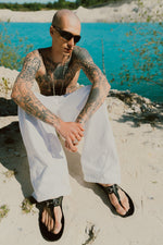 Pleated White Jeans worn by male model seated at a chalk quarry lake — Confession Road campaign