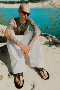 Pleated White Jeans worn by male model seated at a chalk quarry lake — Confession Road campaign
